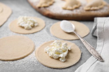Süzme peynirli hamur tatlısı (varenyky) yapma süreci. Çiğ hamur ve malzemeler gri masada, yakın plan.