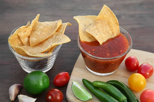 stock image Tasty salsa sauce with tortilla chips and ingredients on wooden table, closeup