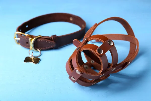 Brown leather dog muzzle and collar on light blue table, closeup