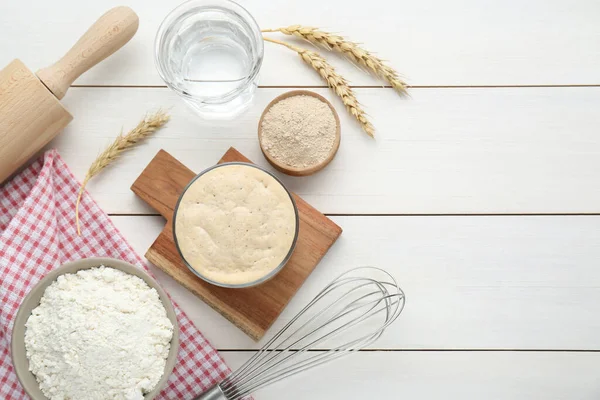 stock image Leaven, flour, water, rolling pin, whisk and ears of wheat on white wooden table, flat lay. Space for text