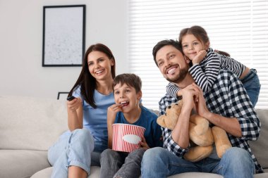 Evde film izleyen mutlu bir aile. Annem uzaktan kumandayla televizyon kanallarını değiştiriyor.