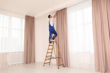 Üniformalı işçiler pencere perdelerini içeri asıyor.