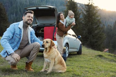 Köpeği olan mutlu bir adam, annesi ve kızı dağlarda arabanın yanında. Aile evcil hayvanla seyahat ediyor