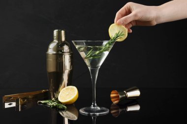 Siyah arka planda limon dilimli Martini kokteyli hazırlayan kadın, yakın plan.