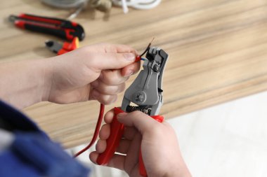 Professional electrician stripping wiring at wooden table, above view