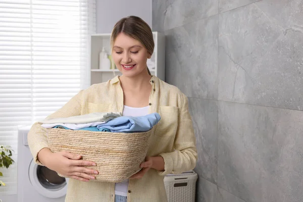 Happy woman with basket full of laundry in bathroom. Space for text