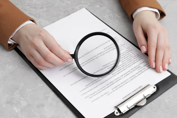 Woman looking at document through magnifier at light gray table, closeup. Searching concept