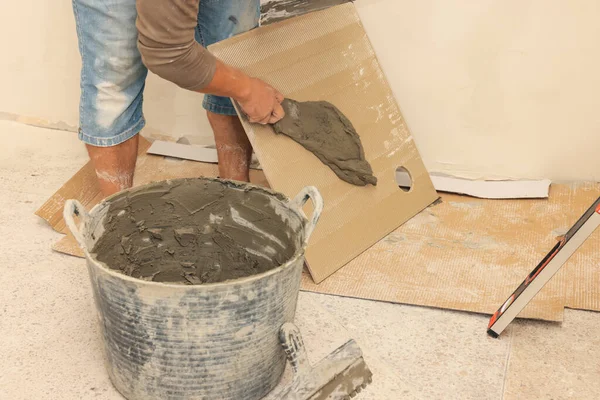 Worker spreading adhesive mix over tile with spatula, closeup