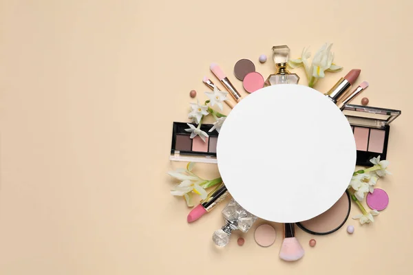 Flat lay composition with different makeup products, blank card and beautiful flowers on beige background, space for text