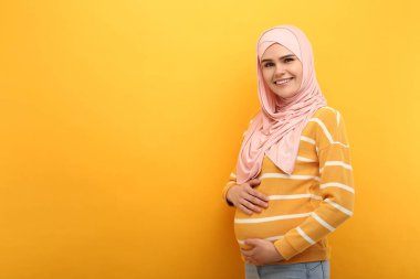 Turuncu arka planda tesettürlü hamile Müslüman kadın portresi, metin için boşluk