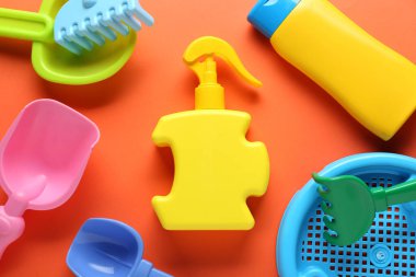 Güneş kremi şişeleri ve turuncu arka planda çocuk plaj oyuncakları.