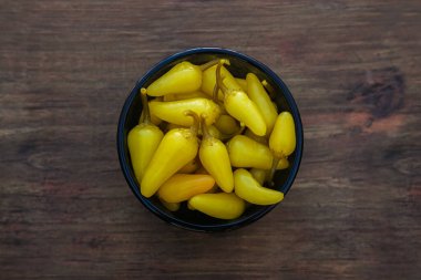 Bowl of pickled yellow jalapeno peppers on wooden table, top view