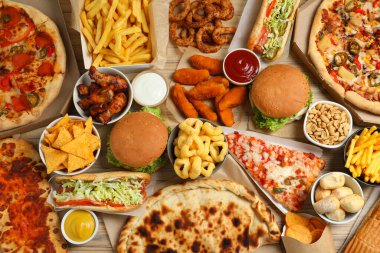 French fries, pizza and other fast food on wooden table, flat lay