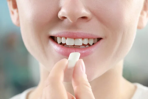 Woman putting chewing gum piece into mouth on blurred background, closeup