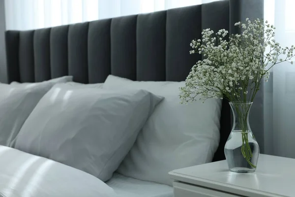 部屋の快適なベッドの近くの白いベッドサイドテーブルの上の美しい花と花瓶 テキストのためのスペース スタイリッシュなインテリア — ストック写真