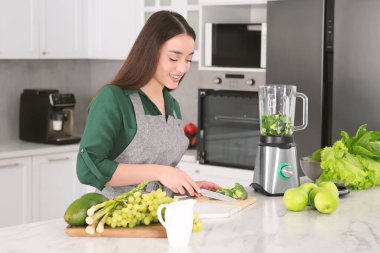 Young woman cutting broccoli for smoothie at white table in kitchen