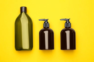 Bottles of shampoo on yellow background, flat lay