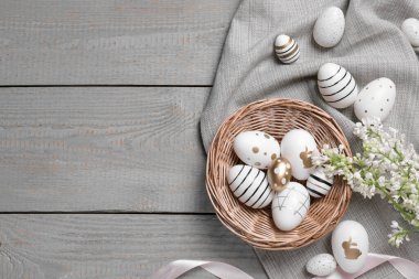Pek çok boyanmış Paskalya yumurtası, leylak çiçekleri ve gri ahşap masa üzerindeki kurdele, düz bir döşeme. Metin için boşluk