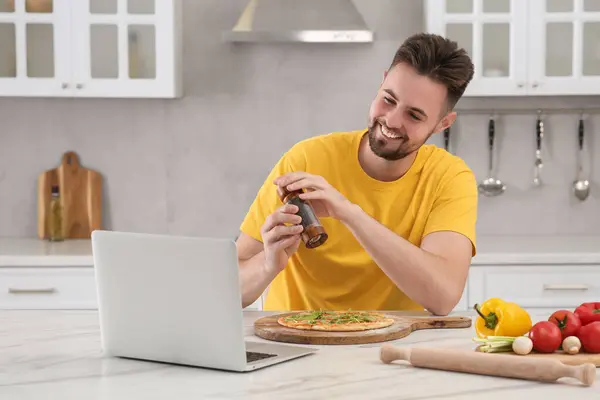 Szczęśliwy Człowiek Dodając Pieprz Pizzy Podczas Oglądania Gotowania Online Kurs — Zdjęcie stockowe