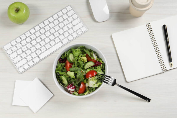 Bowl of tasty food, keyboard, fork, apple and notebook on white wooden table, flat lay. Business lunch