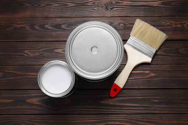 stock image Can of white paint, closed one and brush on wooden table, flat lay