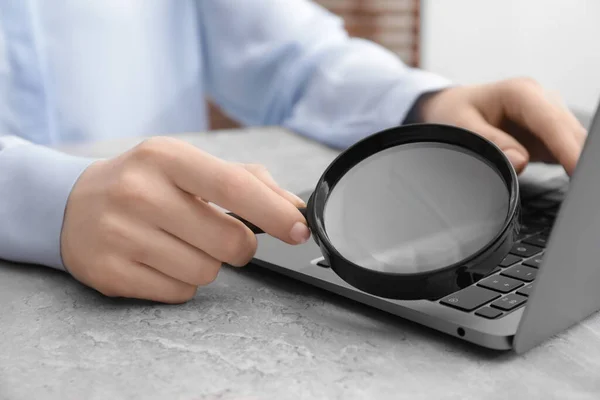 stock image Woman holding magnifier near laptop at light gray table, closeup. Online searching concept