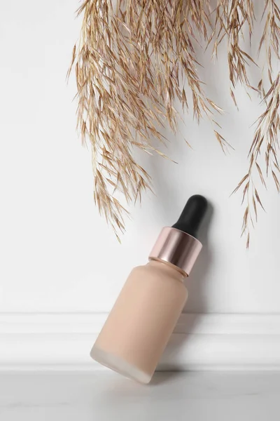 Skin foundation and decorative plant near white wall. Makeup product