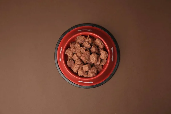 Wet pet food in feeding bowl on brown background, top view