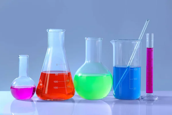 不同的实验室玻璃器皿 白桌上有色彩艳丽的液体 背景灰暗 — 图库照片