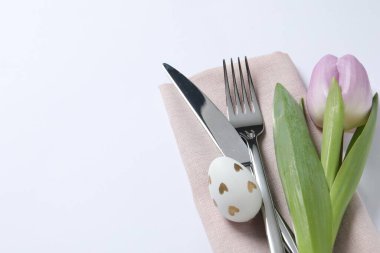 Cutlery set, Easter egg and tulip on white background, space for text. Festive table setting