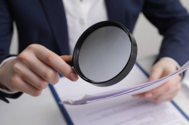 Kadın masadaki büyüteçle belgeye bakıyor, yakın plan. Konsept aranıyor