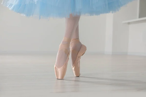 Ballerina in pointe shoes and light blue skirt dancing indoors, closeup
