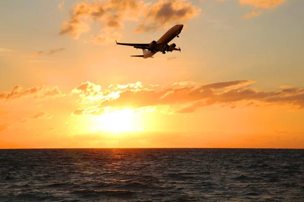 stock image Plane flying over sea during sunset. Sun shining through clouds