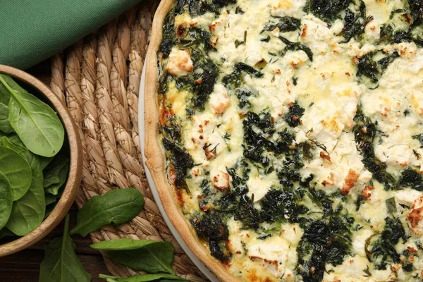 Stock image Delicious homemade quiche and spinach leaves on wicker mat, flat lay