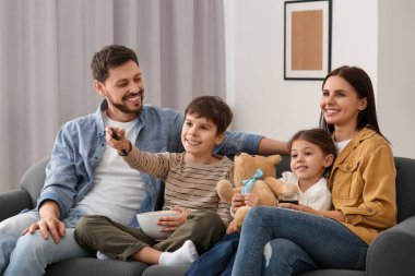 Evde televizyon izleyen mutlu bir aile. Evlat uzaktan kumandayla kanal değiştiriyor