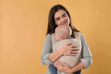 Anne, bej arka planda çocuğunu askıda (bebek taşıyıcısı) tutuyor. Metin için boşluk