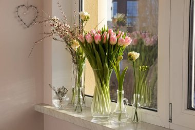 Many different spring flowers and branches with leaves on windowsill indoors