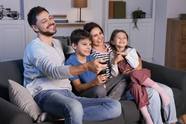 幸せな家族は夕方に家でテレビを見ている お父さん遠隔操作でチャンネルを変える — ストック写真