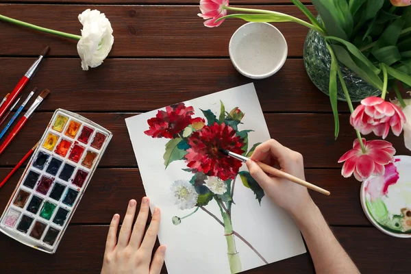 stock image Woman painting flowers with watercolor at wooden table, top view. Creative artwork