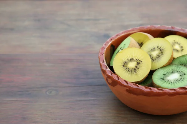 Bowl of many cut fresh kiwis on wooden table, closeup. Space for text