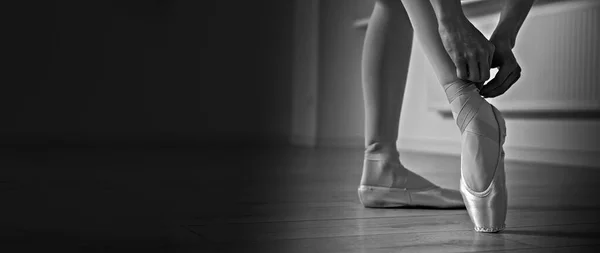 Ballerina tying pointe shoes in dance studio, closeup. Black and white effect. Banner design with space for text