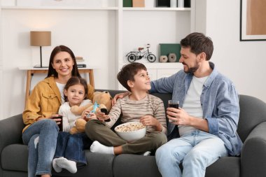Aile evdeki kanepede birlikte vakit geçiriyor. Evlat uzaktan kumandayla TV kanallarını değiştiriyor