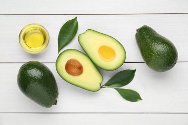Yağlı kase, olgun taze avokado ve beyaz ahşap masa üzerinde yapraklar, düz yatıyordu.