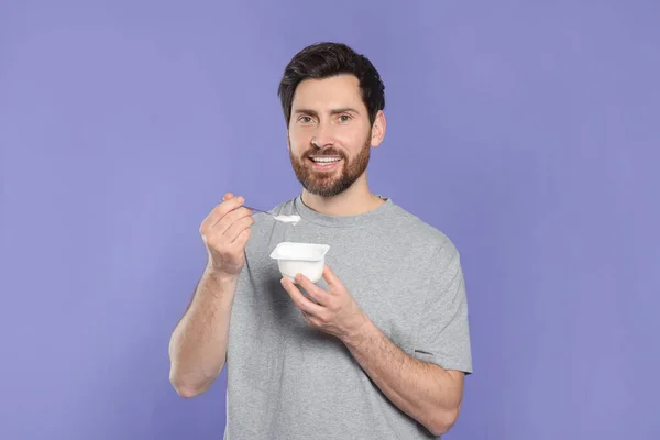 一个英俊的男人 有美味的酸奶和紫色背景的汤匙 — 图库照片
