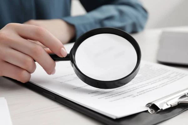 Woman looking at document through magnifier at white wooden table, closeup. Searching concept