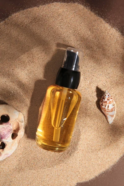 stock image Bottle of serum, seashell and stone on sand against brown background, flat lay