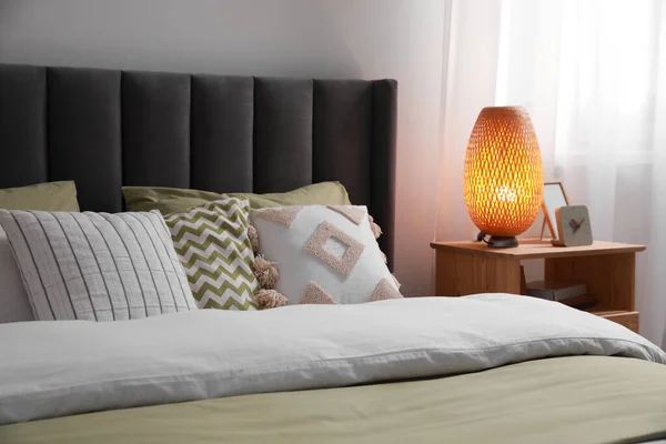 クッション ランプと部屋の木製のベッドサイドテーブルの異なる装飾が施された快適なベッド スタイリッシュなインテリア — ストック写真