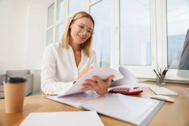 Ofisteki ahşap masada belgelerle çalışan mutlu kadın.