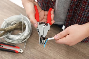 Professional electrician stripping wiring at wooden table, above view
