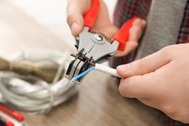 Professional electrician stripping wiring at wooden table, closeup